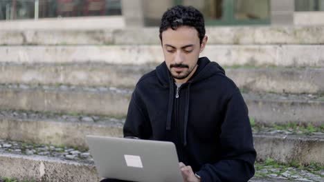 Serious-young-man-using-laptop-on-street